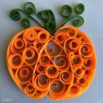 A swirled pumpkin is made of carrot slices and cucumber strips rolled into spirals and artfully arranged on a light surface.