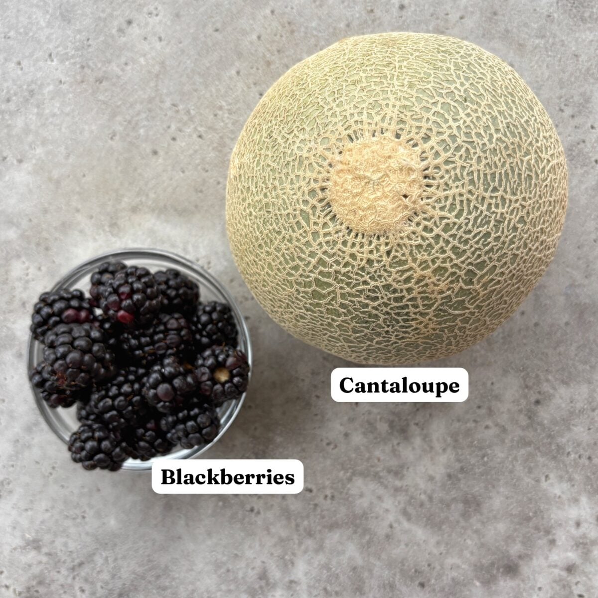 A cantaloupe next to a small glass bowl of blackberries.