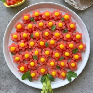 A round plate displays a delightful fruit bouquet of flower-shaped watermelon slices topped with yellow mango balls.