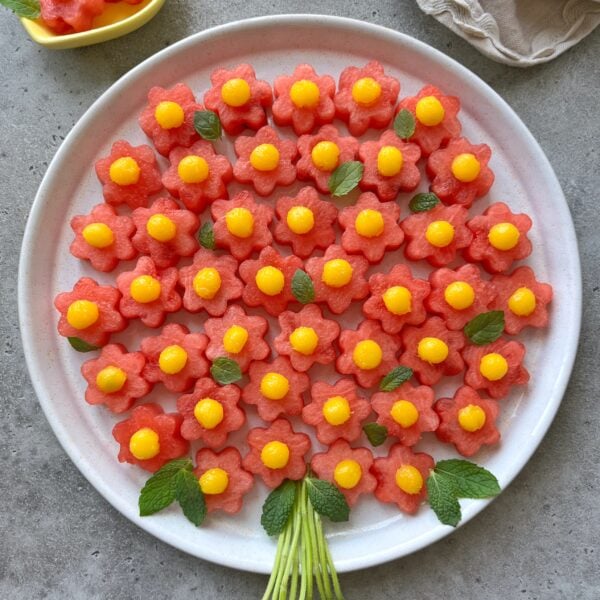 A round plate displays a delightful fruit bouquet of flower-shaped watermelon slices topped with yellow mango balls.