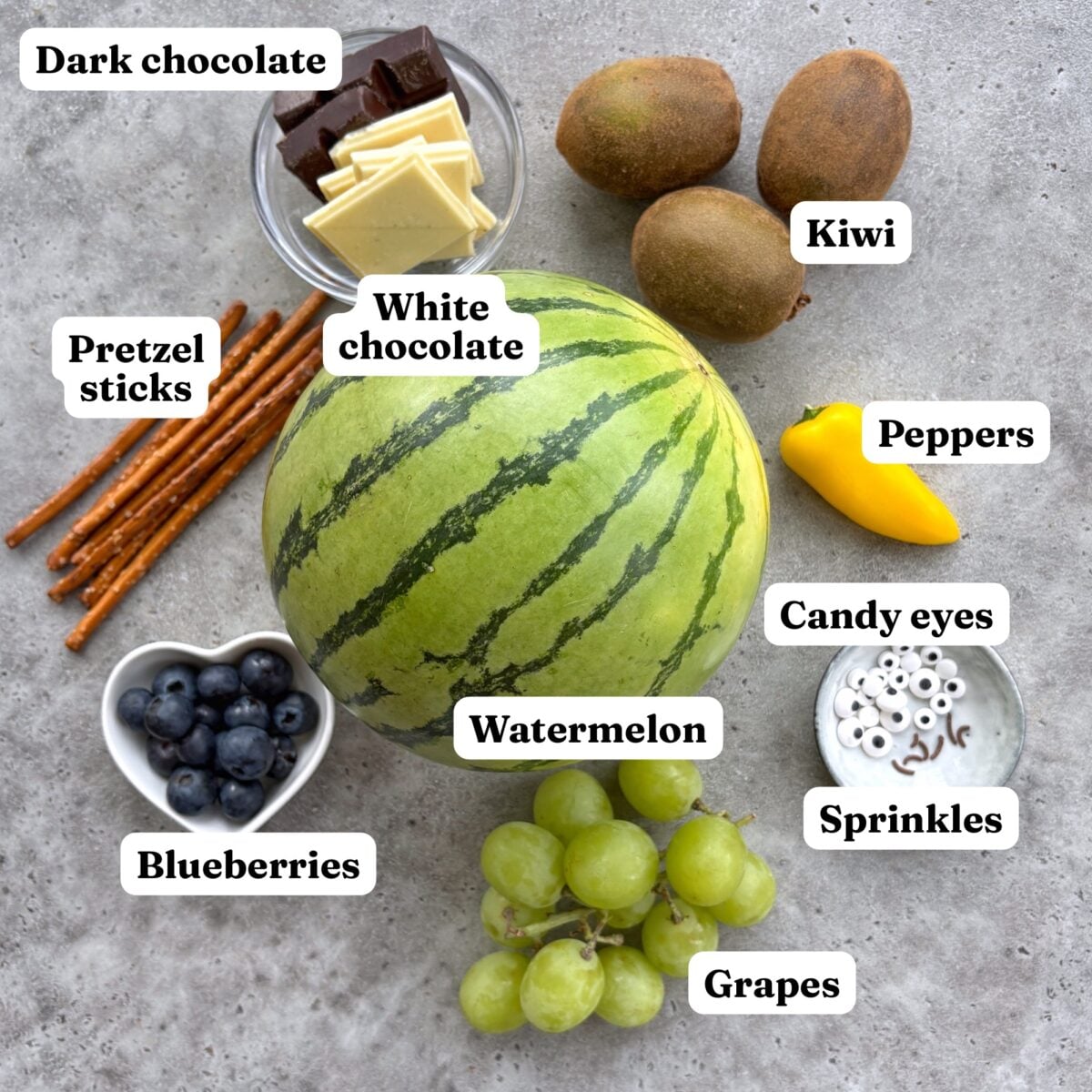 Watermelon, grapes, blueberries, kiwi, peppers, pretzel sticks, dark and white chocolate, and candy eyes.