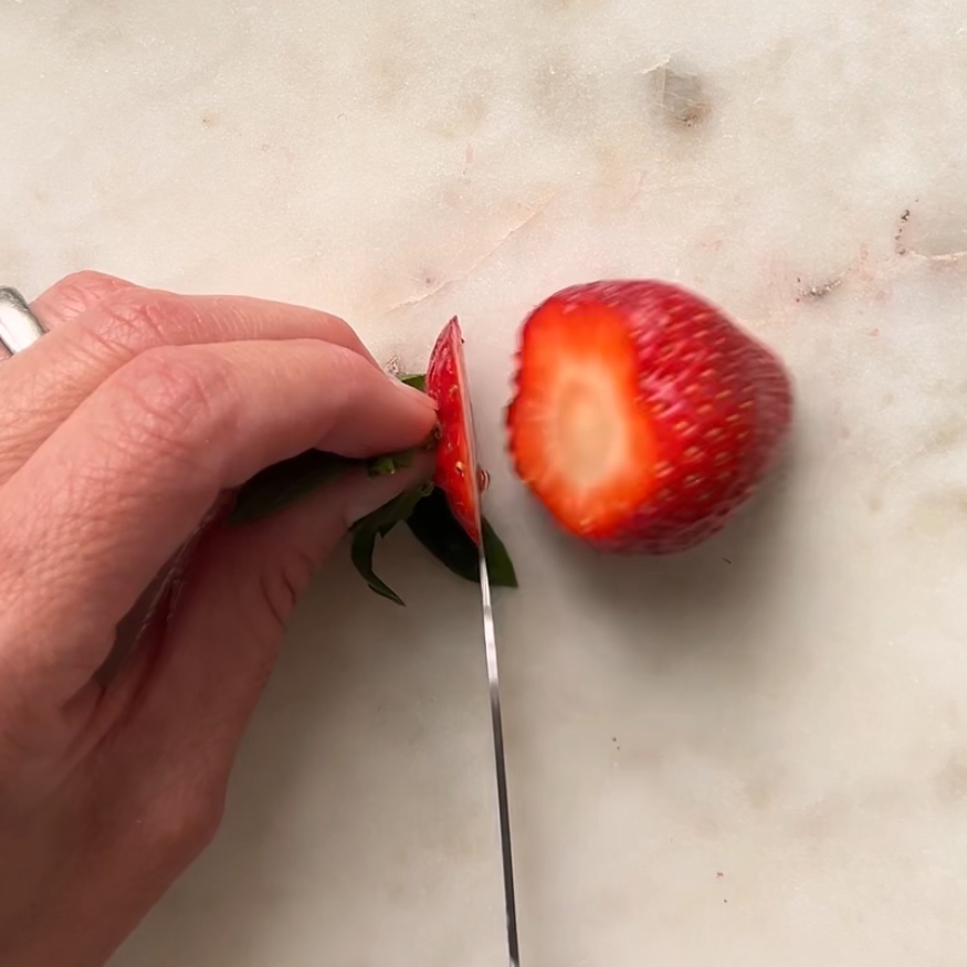A knife trims off the base and leaves on a strawberry.