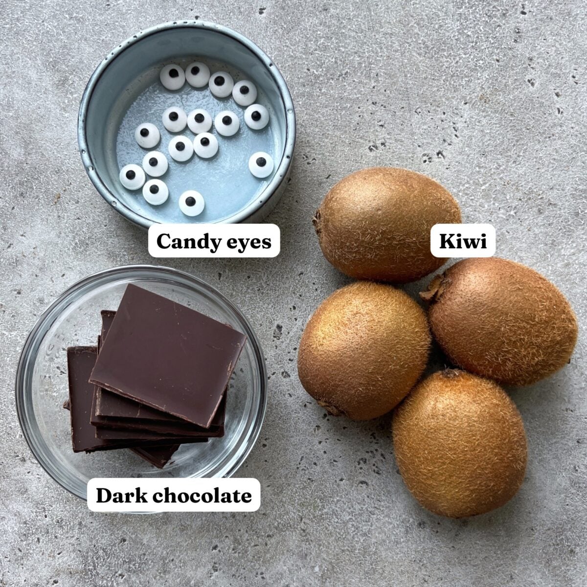 A bowl of candy eyes, a bowl of dark chocolate squares, and four kiwis.