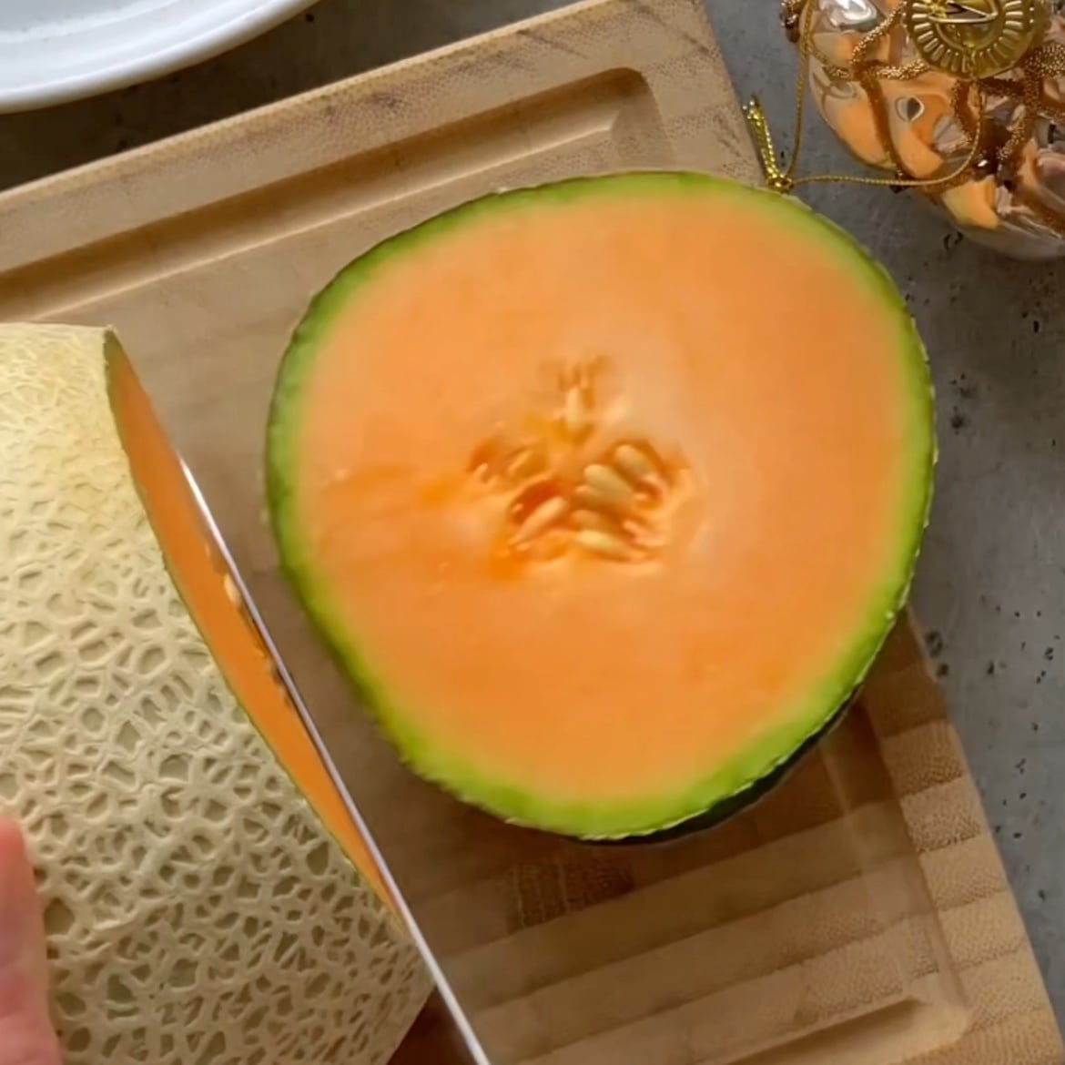 A cantaloupe slice on a wooden cutting board, showing the orange flesh and seeds inside.