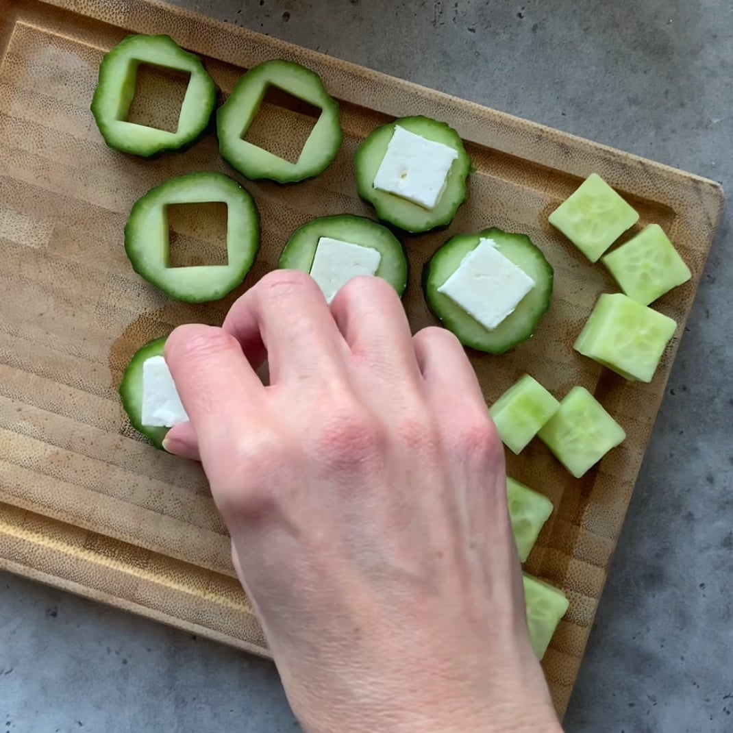 A hand arranges a cube of feta inside the pieces of cucumber.