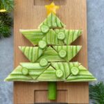 A festive bite, this sandwich is arranged in the shape of a Christmas tree, topped with cucumber slices and a yellow pepper star—perfect for adding creativity to your holiday food recipes. Served on a wooden board.
