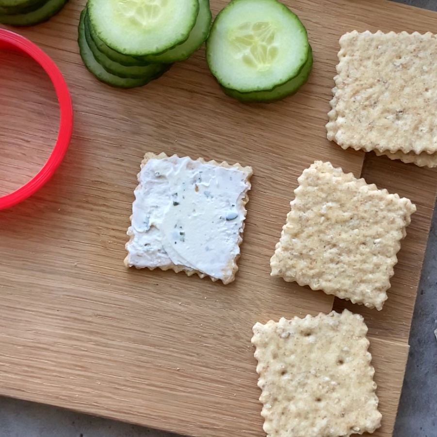 Square crackers on a wooden board, one topped with cream cheese.