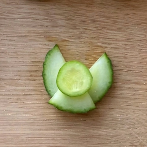 Cucumber slices arranged as an angel on a wooden surface.