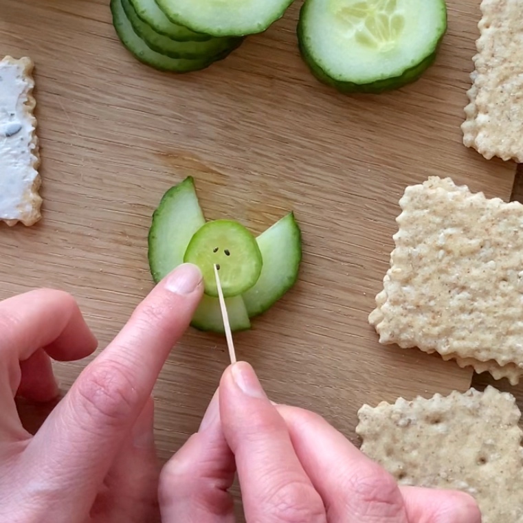 A person uses a toothpick to place seeds on a cucumber slice.