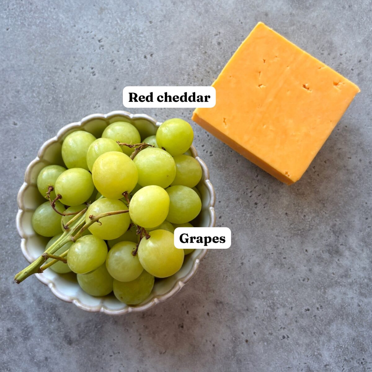 A bowl of green grapes next to a block of red cheddar cheese.