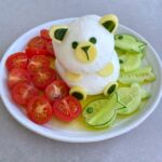 A plate with polar bear-shaped mozzarella cheese surrounded by sliced cherry tomatoes and cucumber slices.