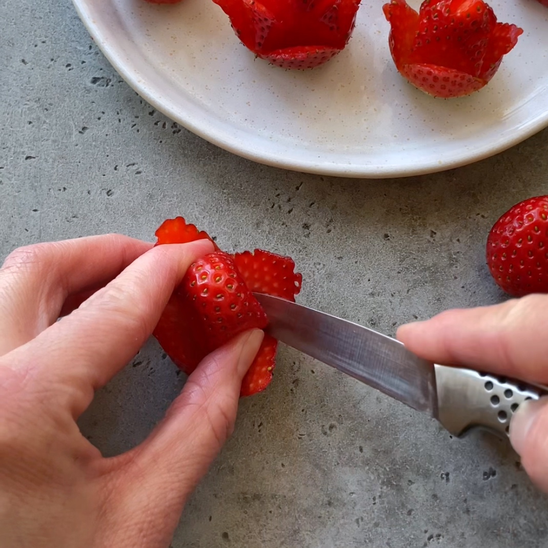 A person uses a knife to carve a strawberry into a flower shape.