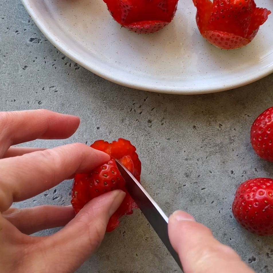 A hand uses a knife to cut a second row of strawberry petals.