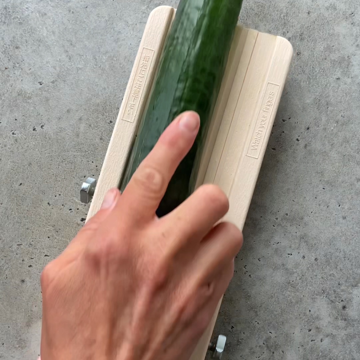 A hand slices a cucumber on a mandolin.