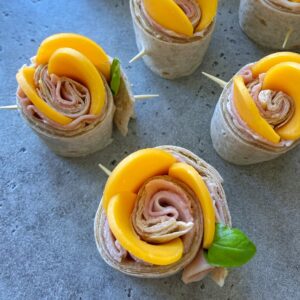 Several tortilla pinwheels filled with ham and sliced yellow bell pepper, secured with toothpicks, are arranged on a gray surface—perfect as tasty bites for parties or healthy additions to your favorite food recipes.