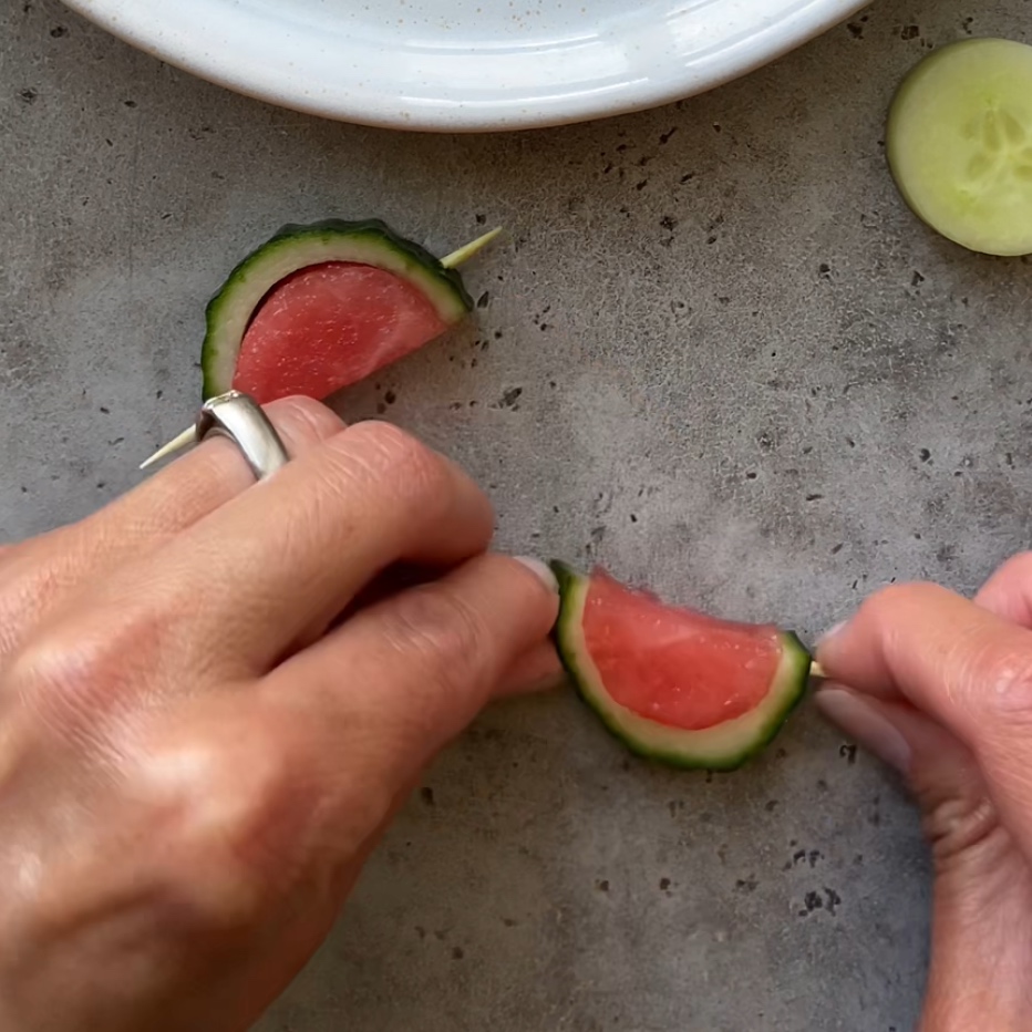 Hands assembling Mini Watermelon Snacks with slices of cucumber and watermelon.