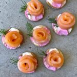 Round tortillas topped with pink and white cream cheese, salmon rosettes, and small sprigs of dill.