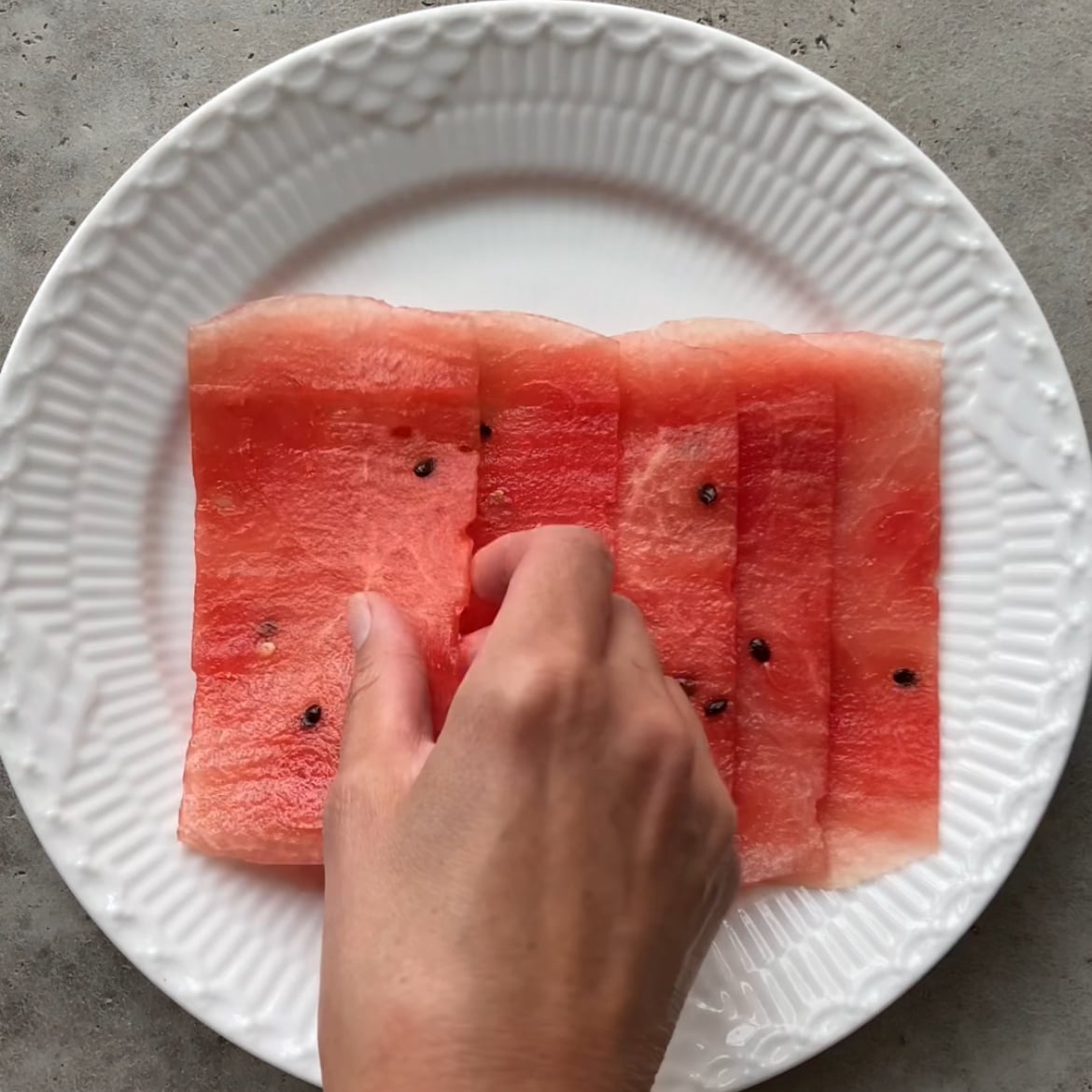 A hand arranges thin slices of watermelon on a platter.