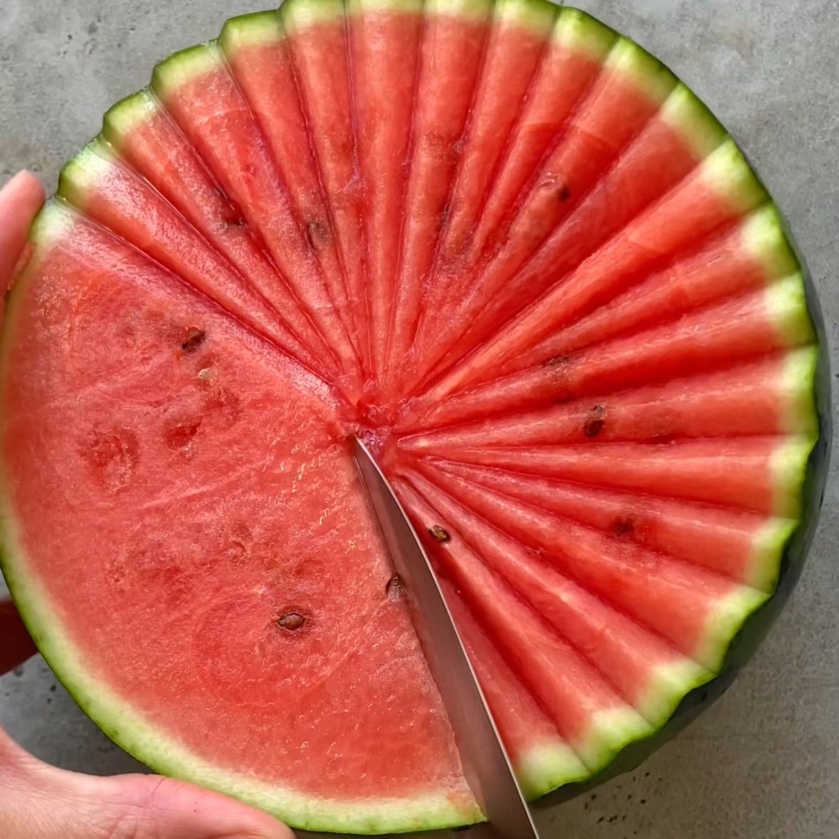 A knife slices an angled cut into a watermelon.