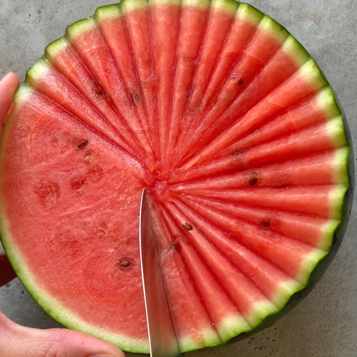 A hand cuts at an angle into a piece of watermelon.