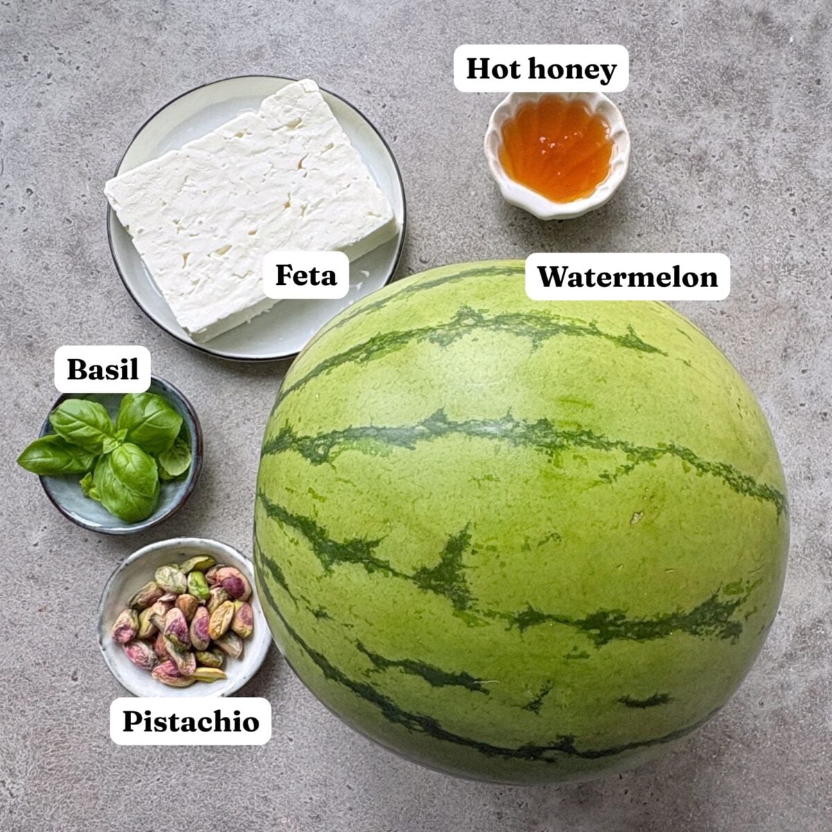 A whole watermelon, a block of feta cheese, fresh basil, pistachios, and hot honey.