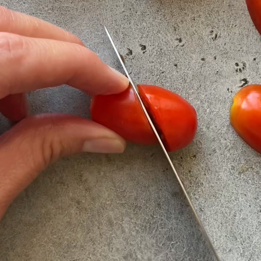 A knife slices a grape tomato in half at a 45 degree angle.