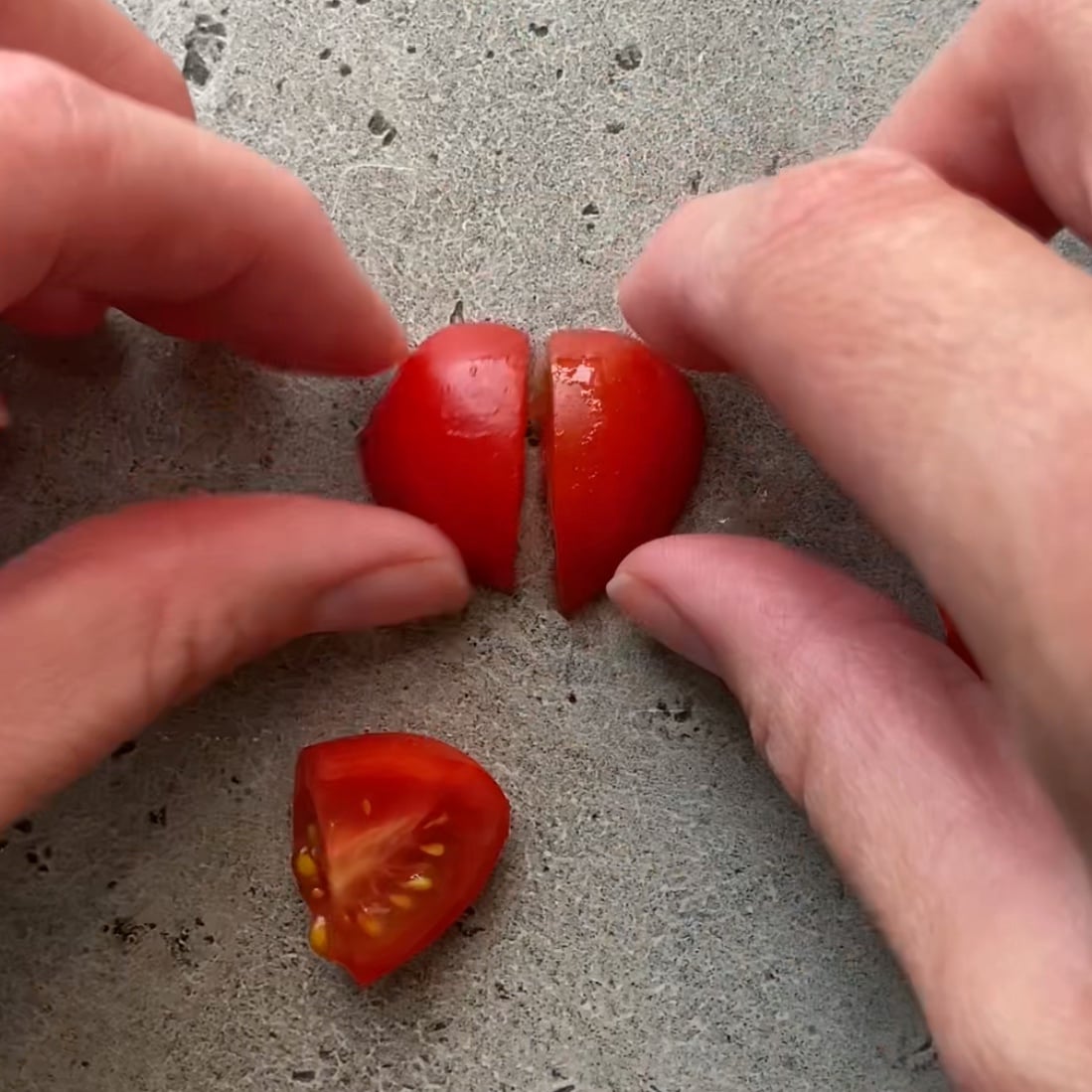 Two halved pieces of grape tomatoes are being matched to make a heart shape.