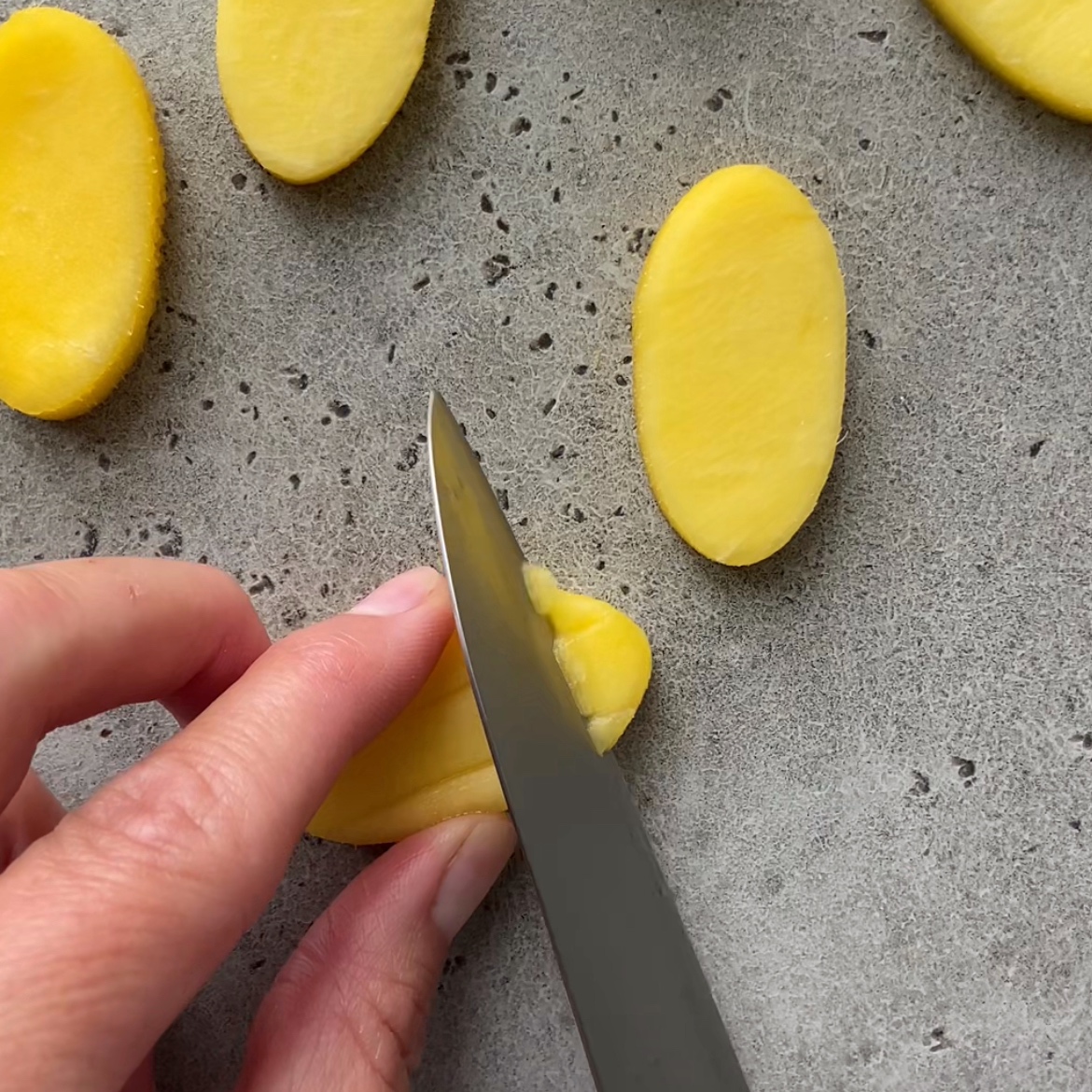 A hand slices scores the top of a small oval-shaped piece of mango.