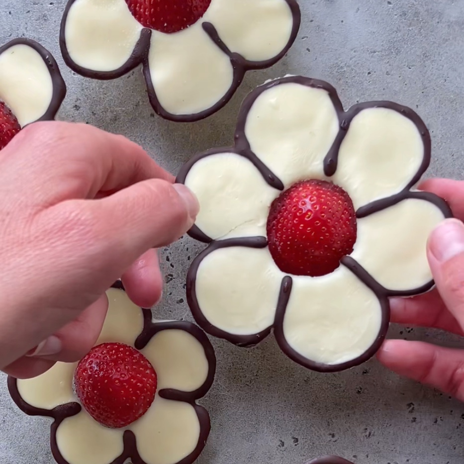 A hand arranges a flower-shaped treat made out of white chocolate with a strawberry center.