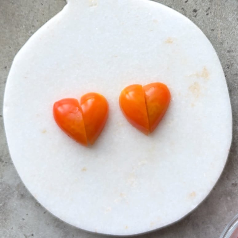 Two orange heart-shaped tomatoes, each split in half, are placed side by side on a round white surface.