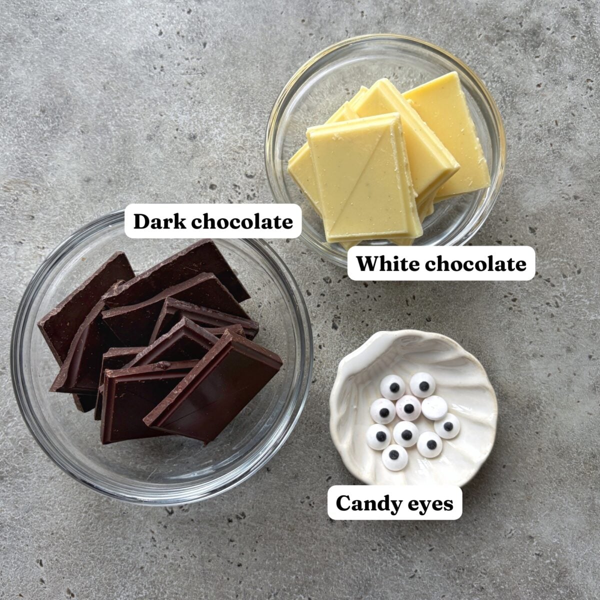 Glass bowls containing dark chocolate squares, white chocolate squares, and candy eyes.