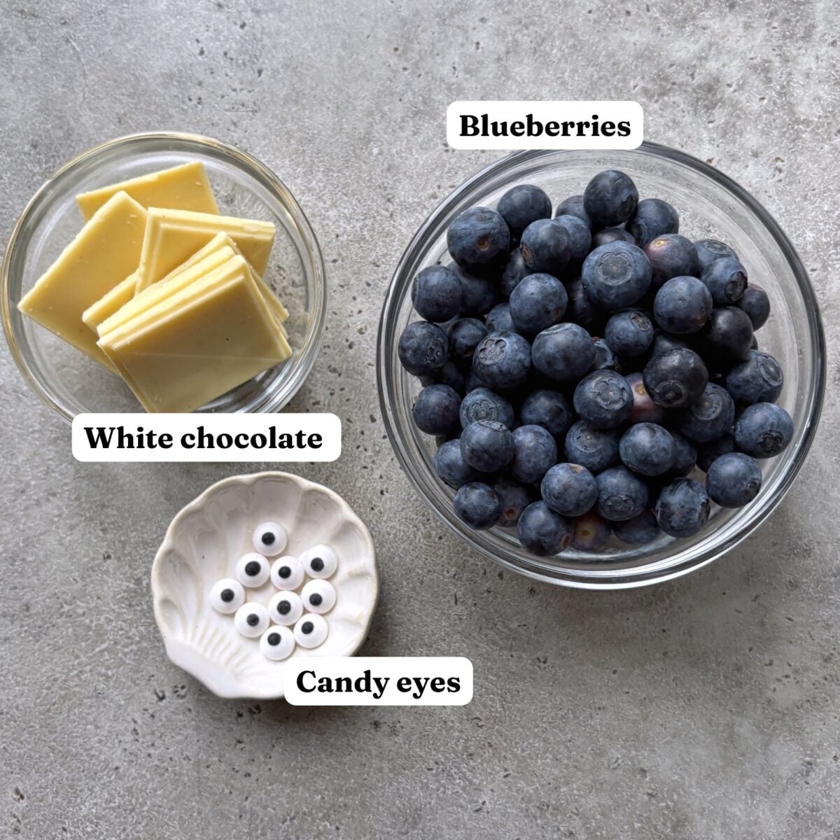 Glass bowls containing white chocolate squares, fresh blueberries, and candy eyes.