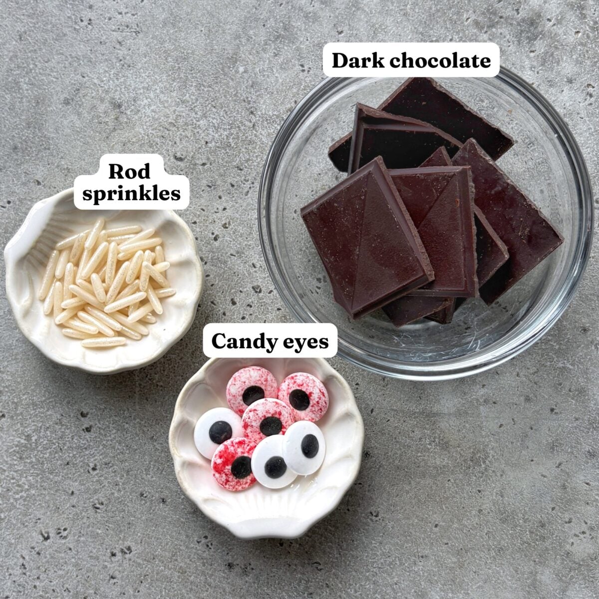 A glass bowl of dark chocolate and small bowls of rod sprinkles and candy eyes.