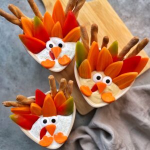 Three bowls of dip are decorated with vegetables and breadsticks arranged to resemble turkeys with carrots, peppers, and candy eyes.