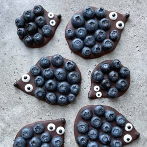 No-Bake Chocolate Hedgehog Treats shaped with blueberries and candy eyes are arranged to resemble hedgehogs on a grey textured surface.
