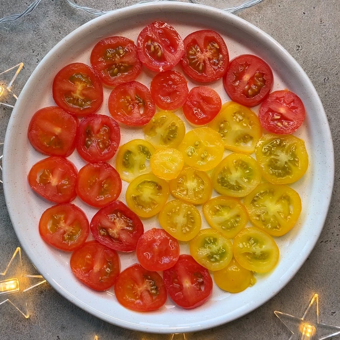 A white plate with sliced red and yellow cherry tomatoes arranged in a gradient pattern.
