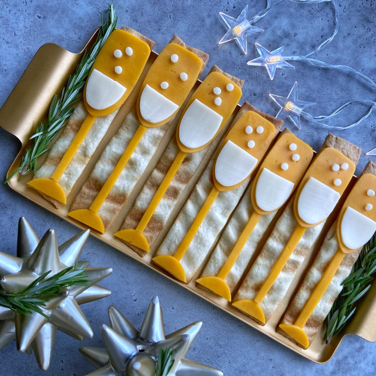 A tray of flat crackers topped with red and white cheddar decorations arranged to look like champagne glasses.