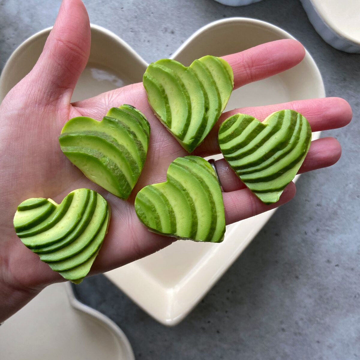 A hand holding five heart-shaped avocado slices.