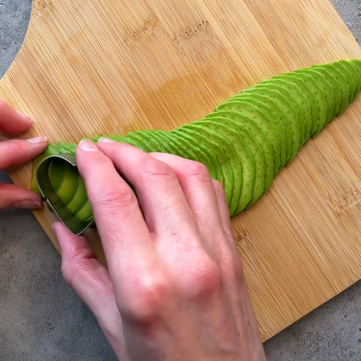 A person uses a heart cookie cutter mold to shape thinly sliced avocado.