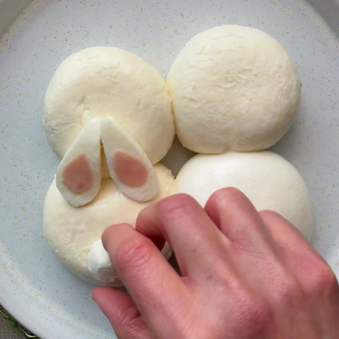 A hand arranges burrata shaped as a bunny on a plate.