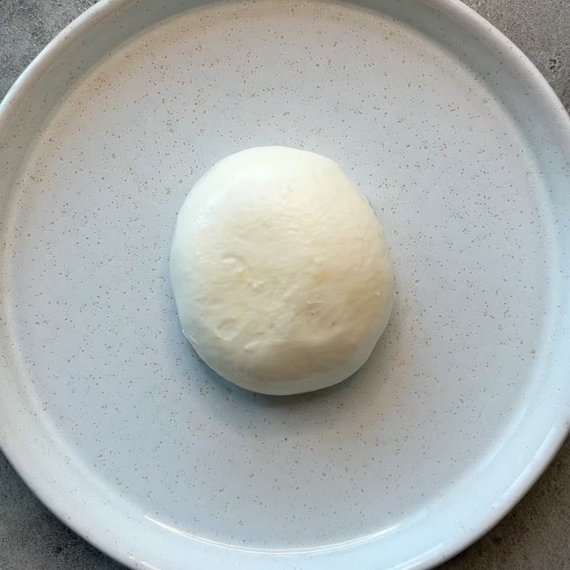 A ball of fresh burrata cheese sits centered on a plain white plate.