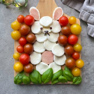 A charcuterie board arranged to look like a bunny, featuring mozzarella, tomatoes, basil leaves.