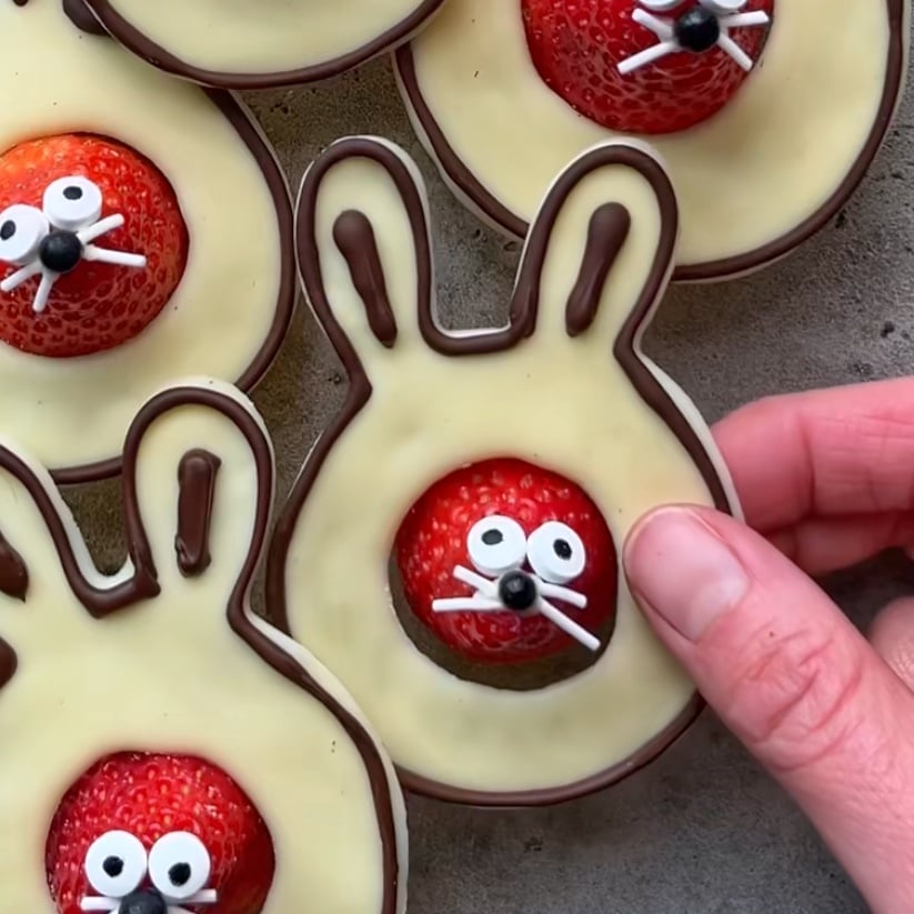 Hand holding a bunny-shaped treat inspired by a classic Chocolate Easter Bunny, featuring a sweet strawberry face, candy eyes, and white chocolate whiskers. More whimsical treats are in the background.
