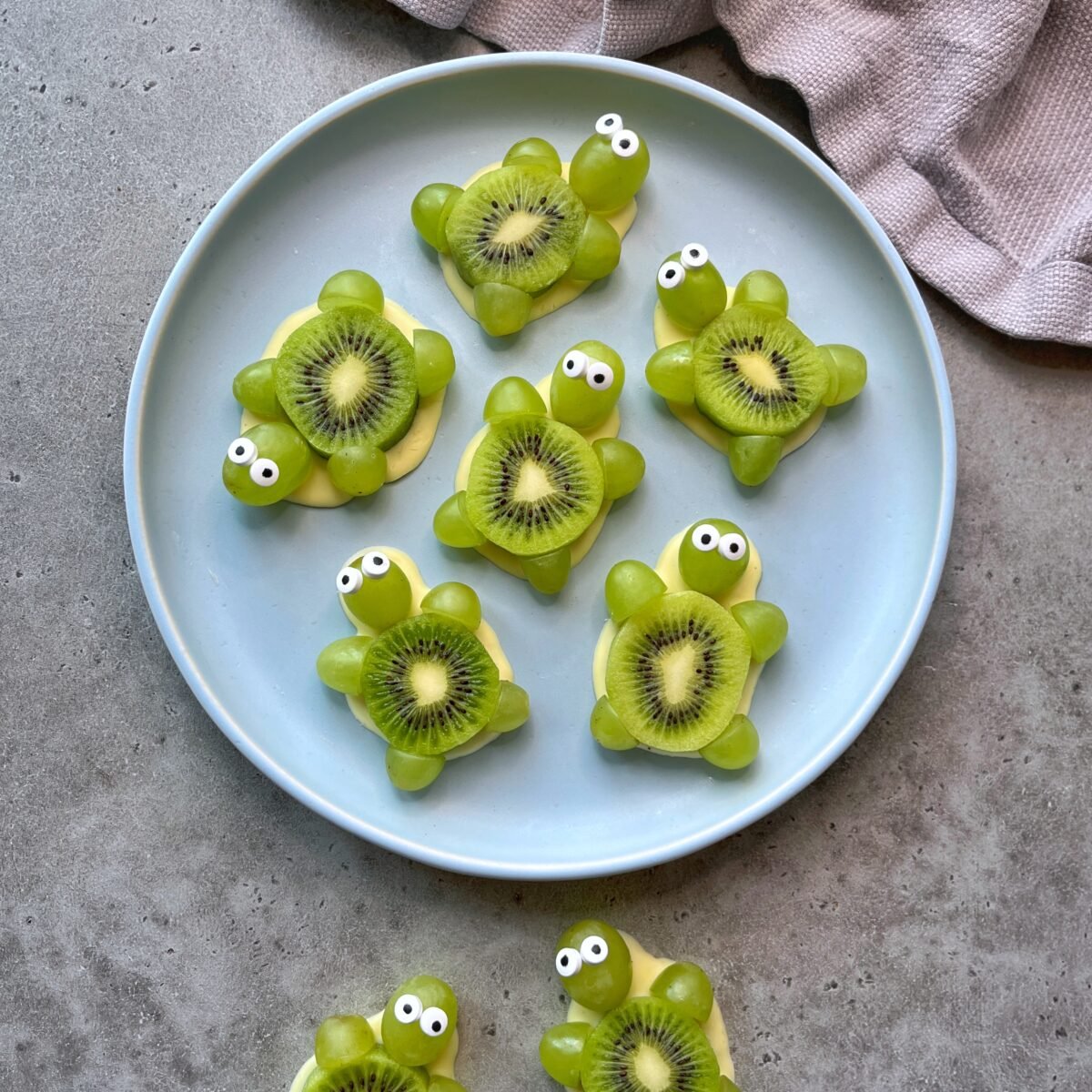 A plate features snacks arranged to look like turtles, made from kiwi slices, green grapes, white chocolate, and candy eyes.