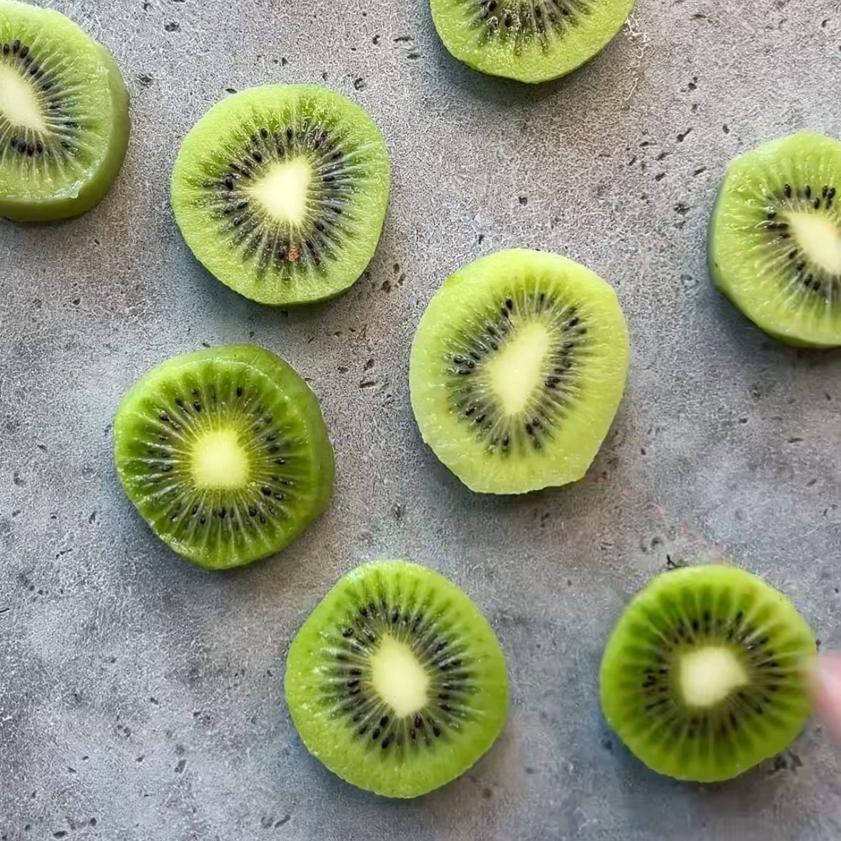 Peeled slices of kiwi arranged on a grey backdrop.