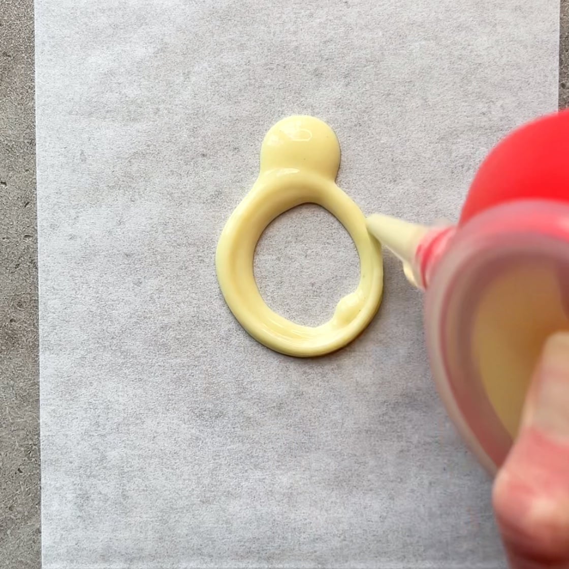 A red piping tool pipes white chocolate onto parchment paper.