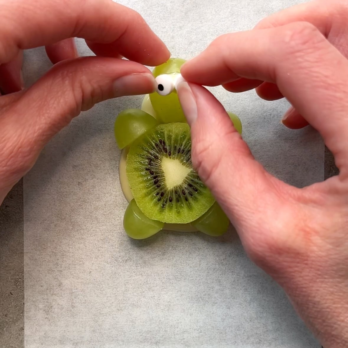 Hands set candy eyes onto a kiwi turtle.