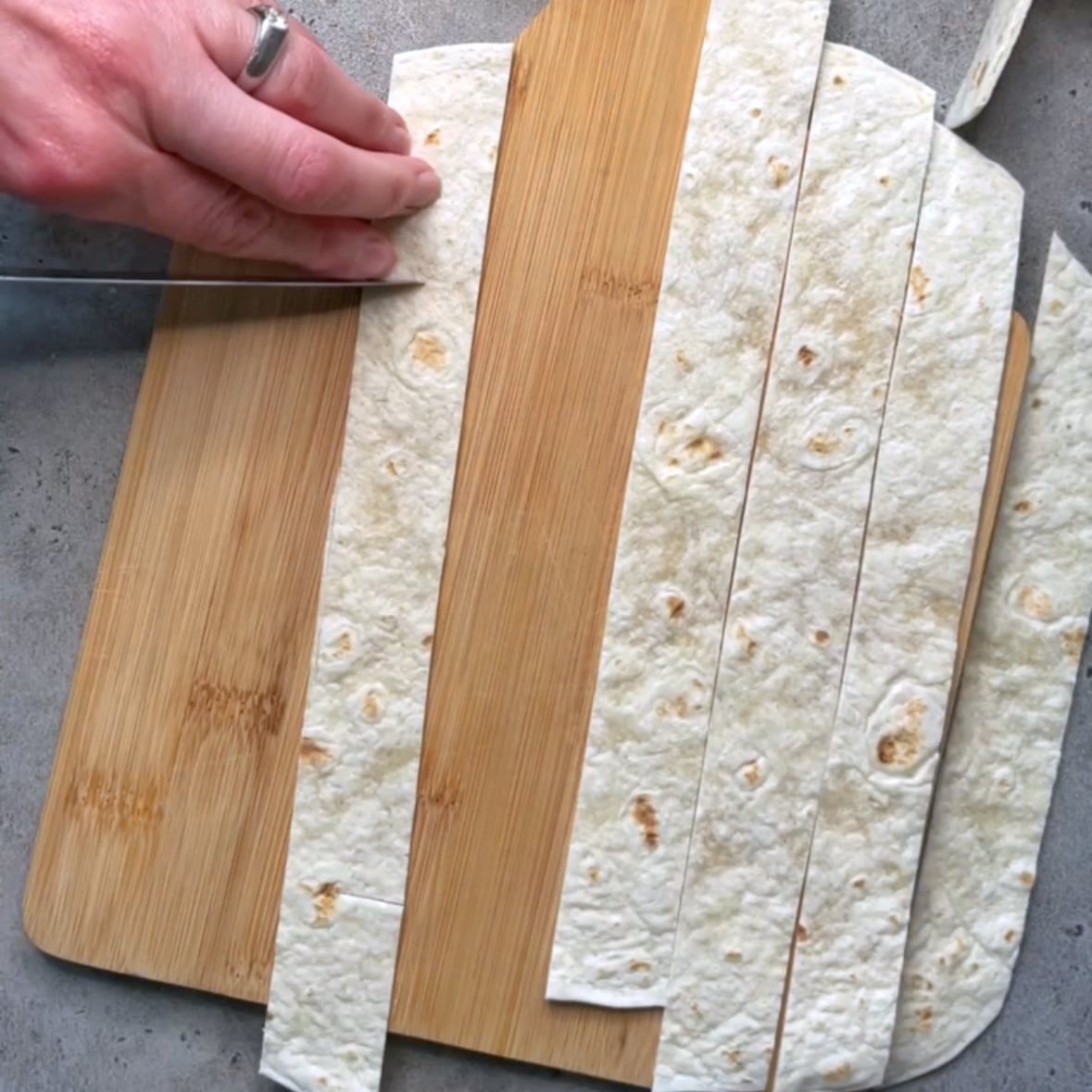 A knife cuts an incision into a strip of tortilla to make tortilla ribbons.