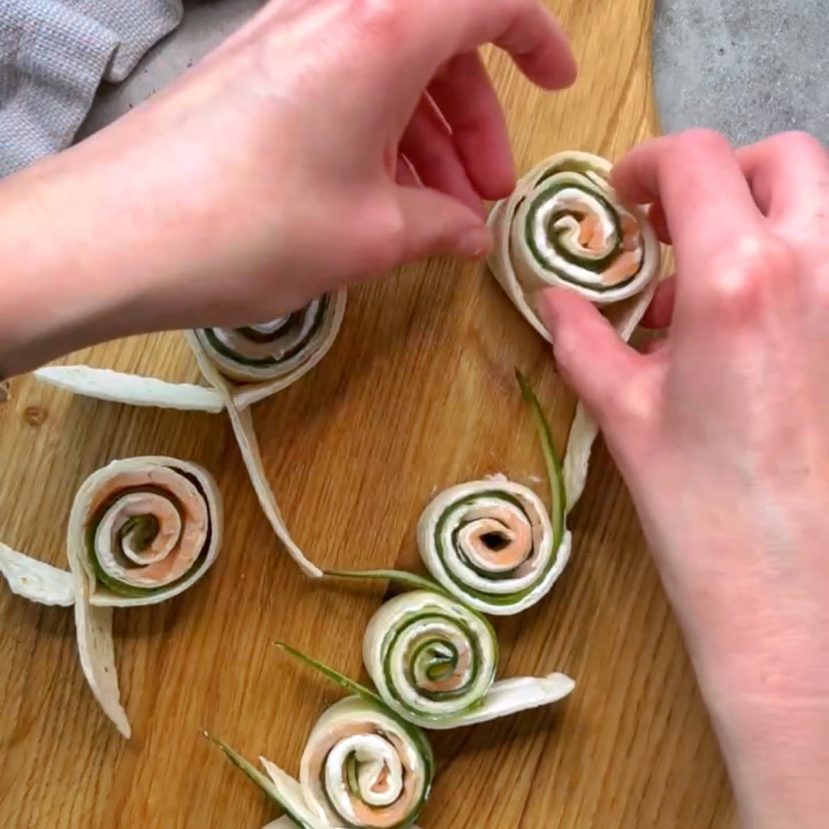 A hand places a smoked salmon and cucumber roll up into a tortilla ribbon to hold them together.