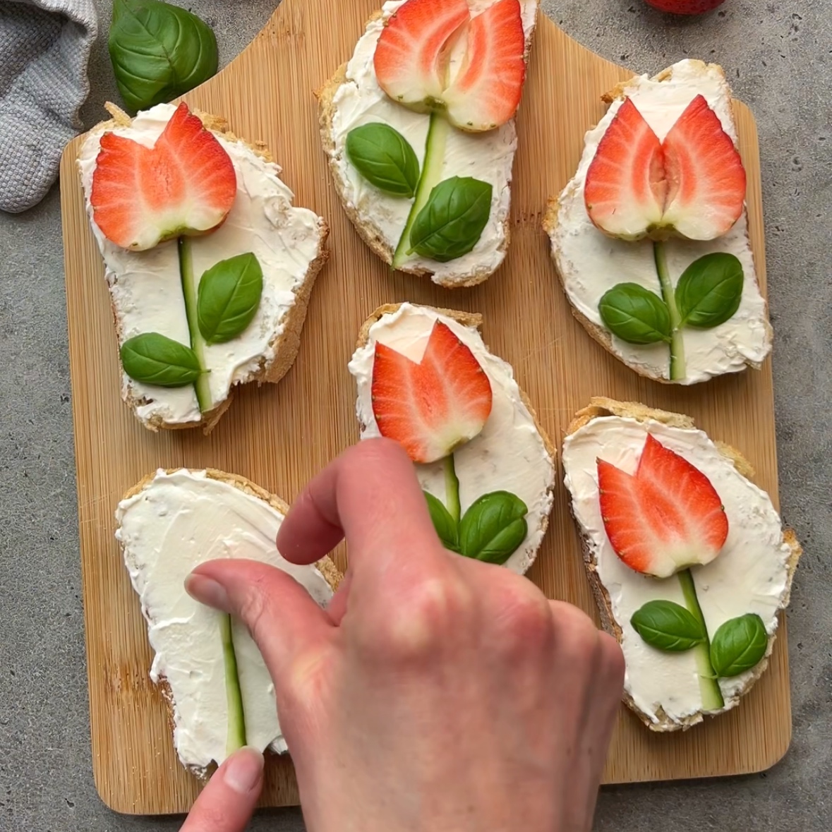 A hand tops bread with a cucumber stem.